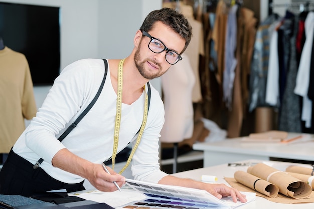 Foto giovane stilista professionista con nastro di misurazione che ti guarda mentre prepara la nuova collezione stagionale in officina