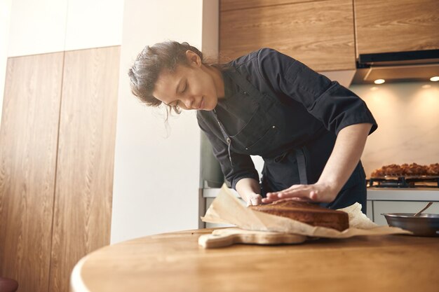 Молодая профессиональная повар готовит вкусный торт на своей светлой современной кухне