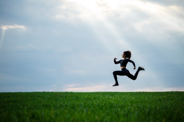 Young professional gymnast is jumping in nature against the blue sky. Girl athlete in a black top and black leggings does acrobatic exercises