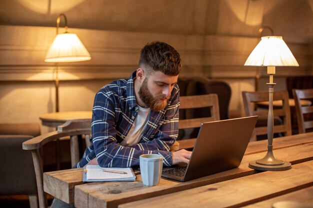 Young professional surfing the Internet on his laptop with cup of coffee on table at coffee shop or home office, working from cafe concept