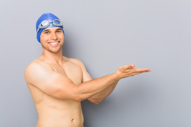 Young professional swimmer man holding a copy space on a palm.
