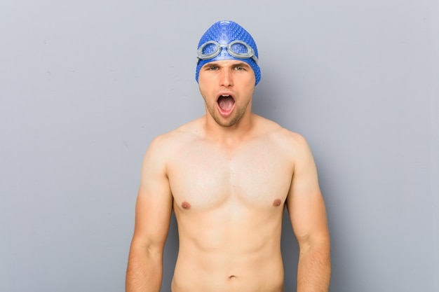 Young professional swimmer man screaming very angry and aggressive.