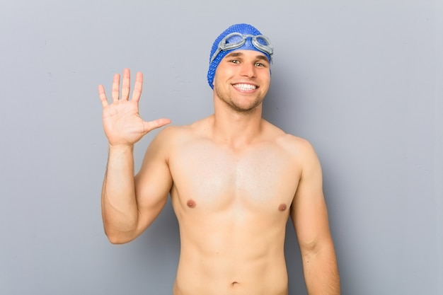 Young professional swimmer man smiling cheerful showing number five with fingers.