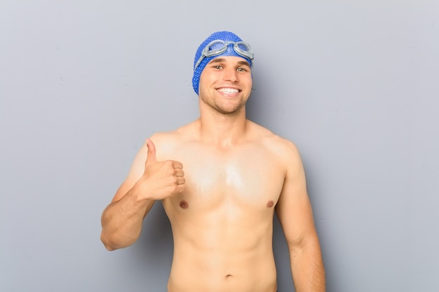 Young professional swimmer man smiling and raising thumb up