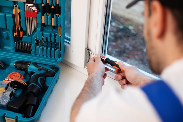 Young professional worker man in uniform suit is installing window with help of tools