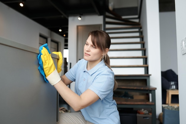 Photo young professional worker in protective gloves wiping dust from furniture during housework