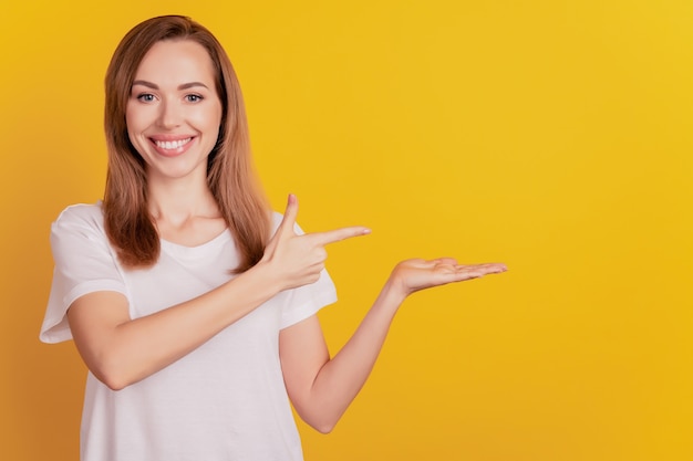 Young promoter woman direct forefinger empty space hold palm toothy smile on yellow wall