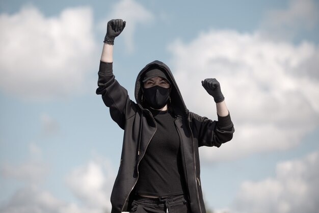 A young Protestant woman raises her hand in the air against a cloudy sky