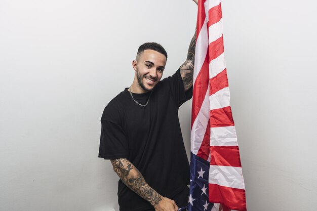 Photo young proud hispanic man holding a us flag against a white background