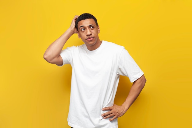 Photo young puzzled african american guy in white tshirt sketches his head with his hand