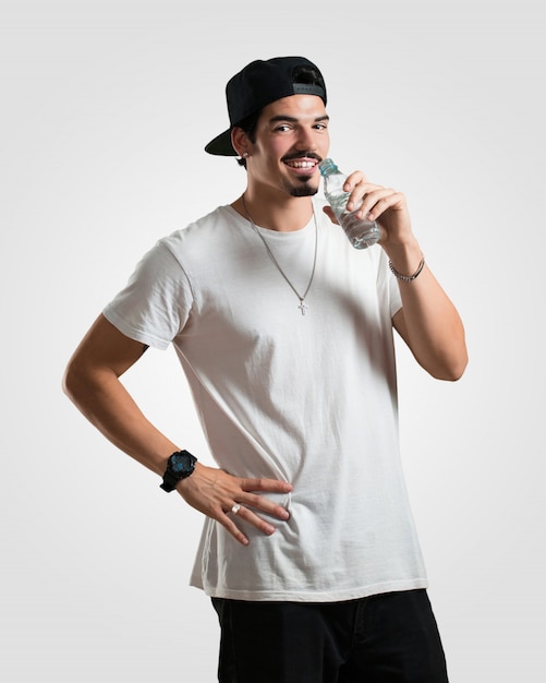 Young rapper man smiling satisfied, holding a bottle of cold water, remembering that hydration is important for the body