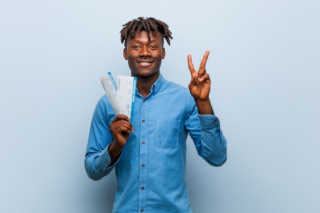 Young rasta black man holding an air tickets showing number two with fingers.