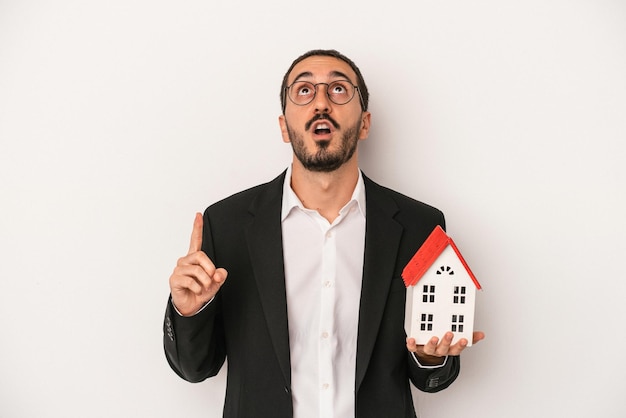 Young real estate agent man holding a model house isolated on white background pointing upside with opened mouth