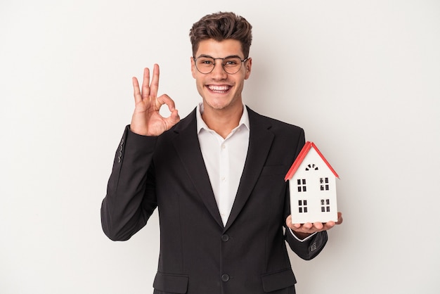 Young real estate caucasian agent isolated on white background cheerful and confident showing ok gesture.