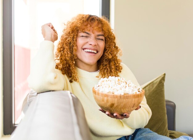 ソファでポップコーンを食べて映画を見ている若い赤毛のラテン系のきれいな女性