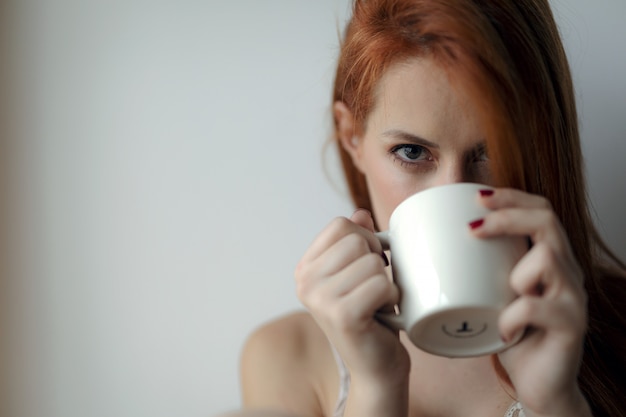 Photo young red hair woman having a hot drink at home