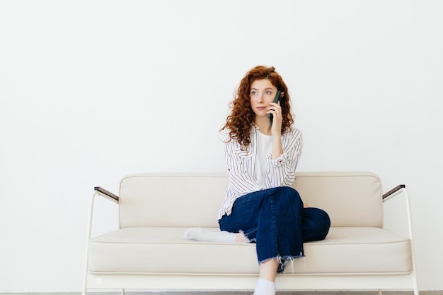 Young red hair woman sitting at home sofa couch drinking coffee talking on mobile phone relaxed in communication and lifestyle concept