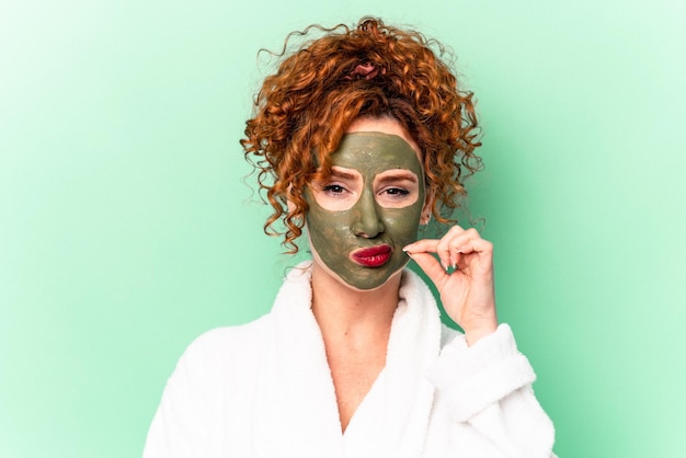 Young red hair woman with a facial aloe vera mask after a bath isolated with fingers on lips keeping a secret