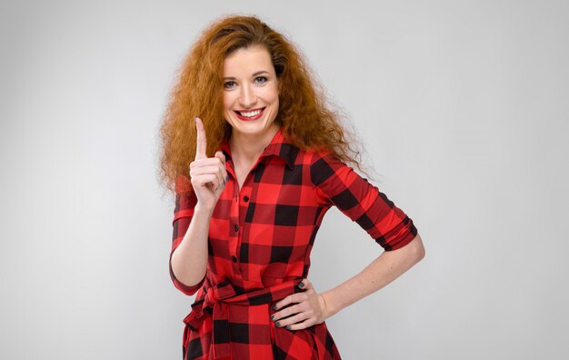 Young red-haired girl in a red checkered shirt. Young girl showing index finger