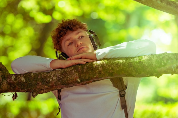 写真 ヘッドフォンで若い赤毛の男は木に寄りかかって立っています