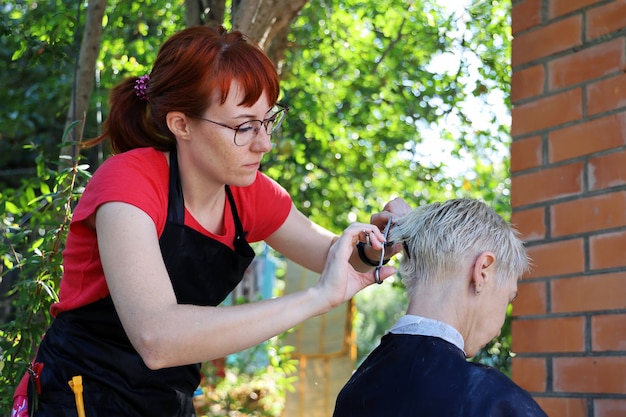 Il giovane parrucchiere della donna dai capelli rossi fa il taglio di capelli corto alla donna all'aperto