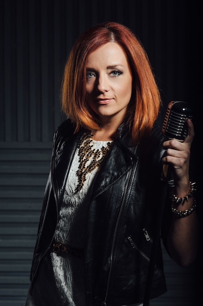 Young red-haired woman in a white dress and a black leather rocker jacket sings emotionally into the microphone