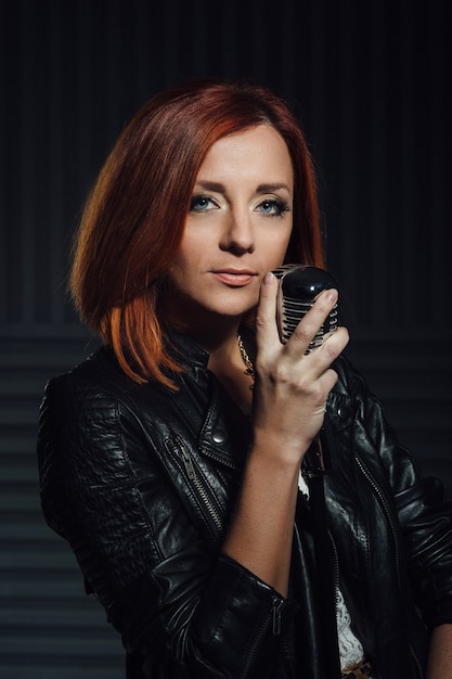 Young red-haired woman in a white dress and a black leather rocker jacket sings emotionally into the microphone