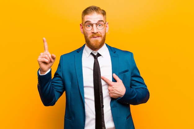 Young red head businessman feeling proud and surprised, pointing to self confidently, feeling like successful number one