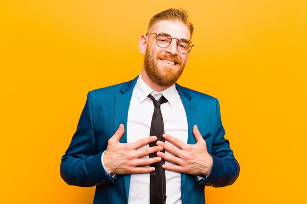 Young red head businessman looking happy, surprised, proud and excited, pointing to self on orange