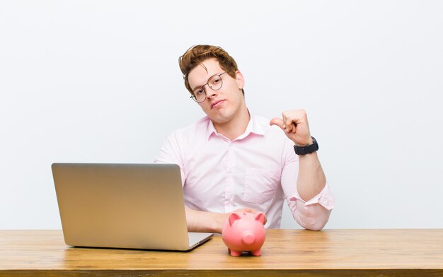 Young red head businessman working in his desk with a piggy bank