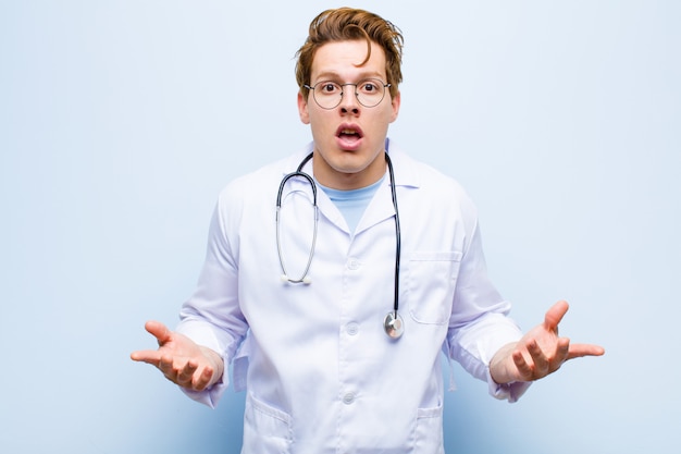 Young red head doctor feeling extremely shocked and surprised, anxious and panicking