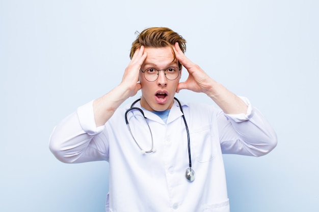 Young red head doctor raising hands to head