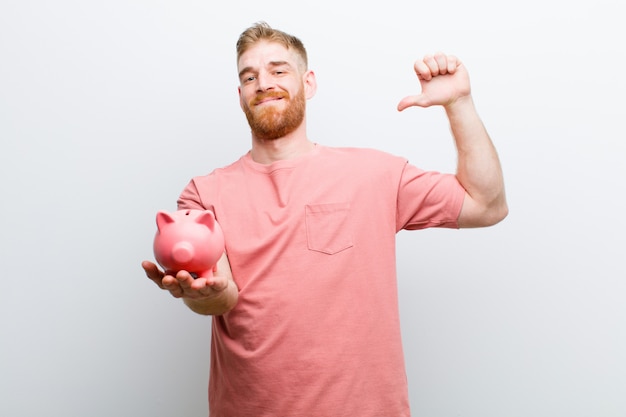 Young red head man holding a piggy bank