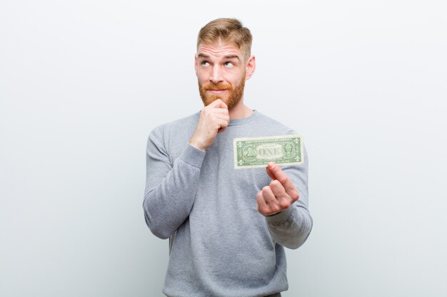 Young red head man with dollars against white background