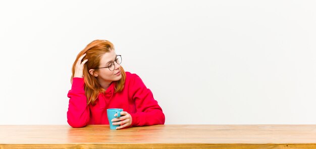 Young red head pretty woman in front of a wooden table with a coffee cup