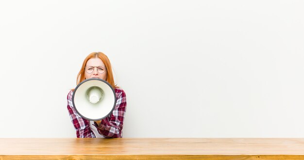 Foto donna graziosa della giovane testa rossa davanti ad una tavola di legno con un megafono