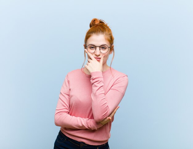 Young red head pretty woman looking serious, thoughtful and distrustful, with one arm crossed and hand on chin, weighting options