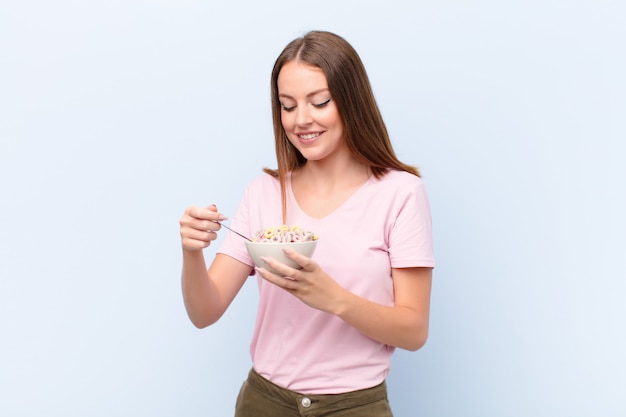 Young red head woman  against flat wall with a breakfast bowl