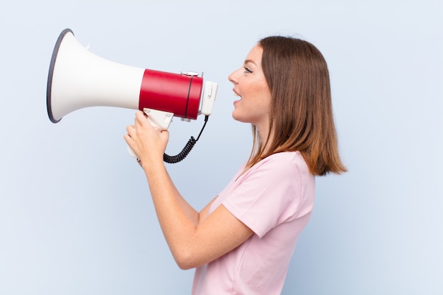 Young red head woman  against flat wall with a megaphone