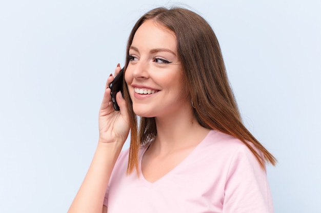 Young red head woman  against flat wall with a smart phone