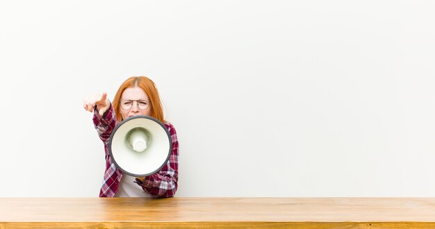 Photo young red head woman in front of a wooden table with a megaphone