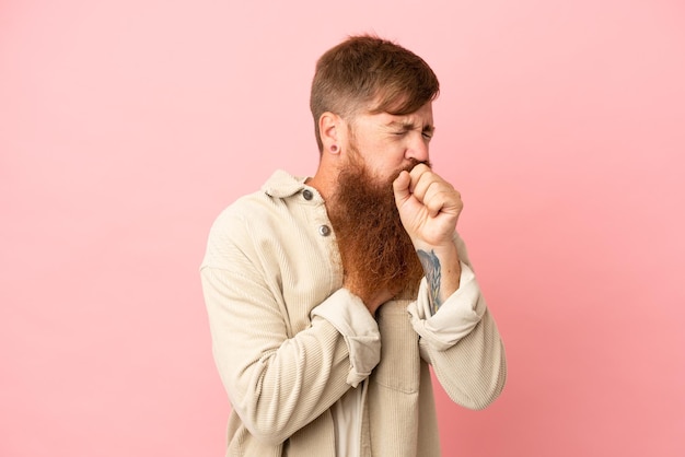 Young reddish caucasian man isolated on pink background coughing a lot