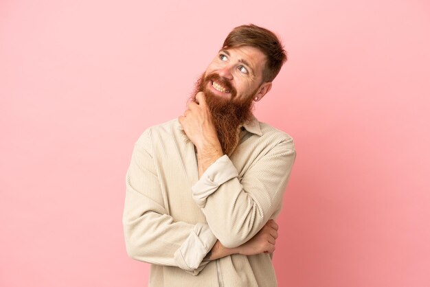 Young reddish caucasian man isolated on pink background looking up while smiling