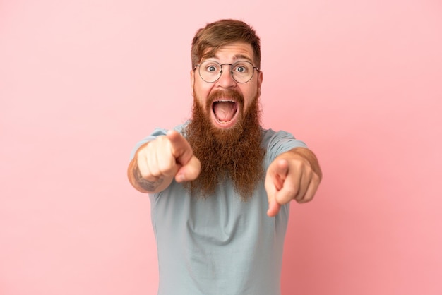 Young reddish caucasian man isolated on pink background surprised and pointing front