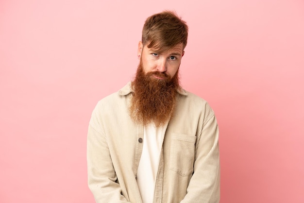 Young reddish caucasian man isolated on pink background with sad expression