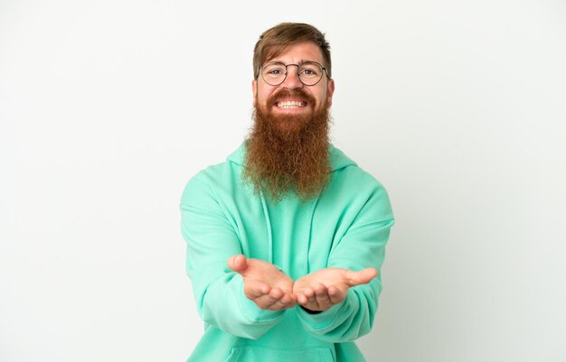 Young reddish caucasian man isolated on white background holding copyspace imaginary on the palm to insert an ad