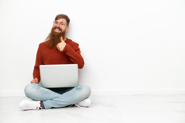 Giovane uomo caucasico rossastro con un computer portatile isolato su sfondo bianco che dà un pollice in alto gesto