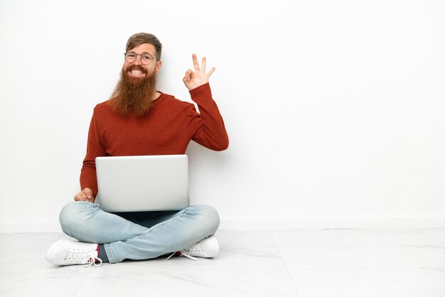 Young reddish caucasian man with laptop isolated on white background showing ok sign with fingers