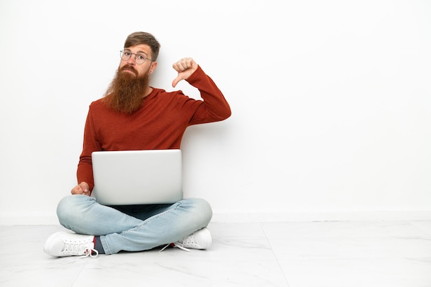 Young reddish caucasian man with laptop isolated on white background showing thumb down with negative expression