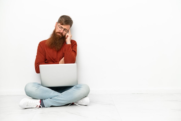 Young reddish caucasian man with laptop isolated on white background with headache